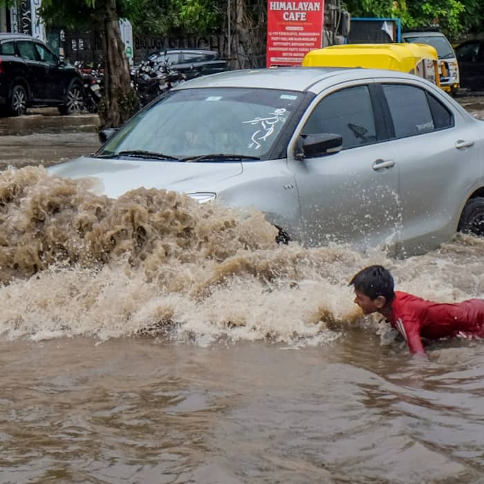 A child plays in a waterlogged area as a car passes by, after heavy rain in Gurugram,