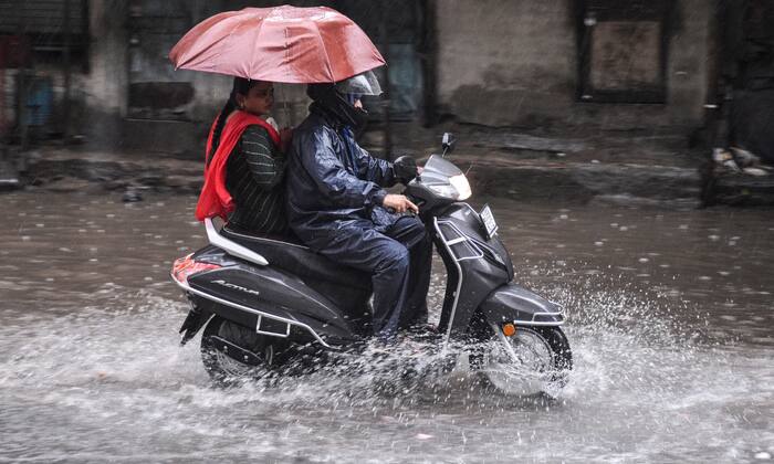 A commuter rides a scooter through a waterlogged road while carrying an umbrella during heavy rain in Surat, Gujarat