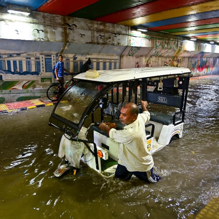 A man pulls his e-rickshaw through a waterlogged road after heavy rain, in Prayagraj,