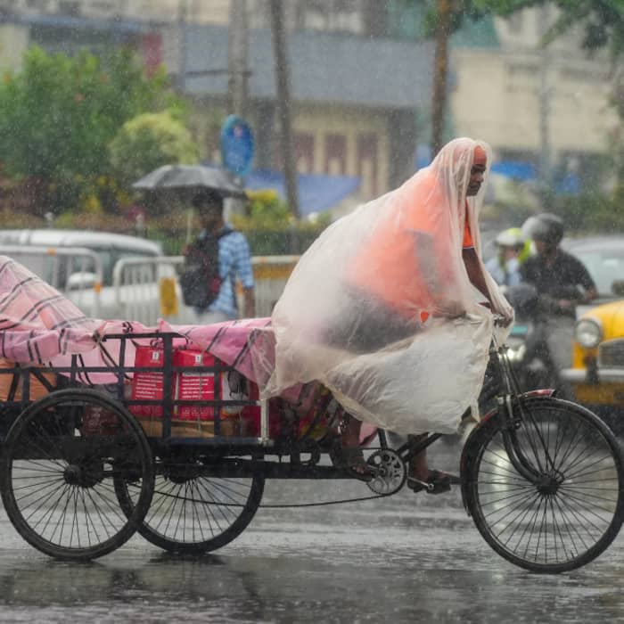 A man travels on a cart covered with a plastic sheet amid rain, in Kolkata, Thursday,