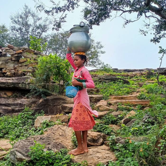 A tribal child carries rainwater collected from an agricultural field in a pot for drinking during the monsoon season, in Bastar district