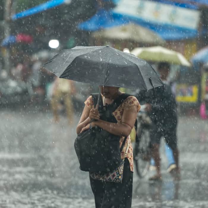 A woman covers her bag and herself amid rain, in Kolkata