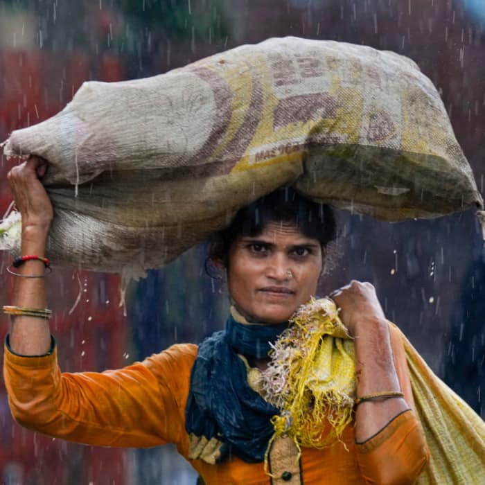A woman wades through a waterlogged road amid rainfall, at Azadpur Mandi, in New Delhi