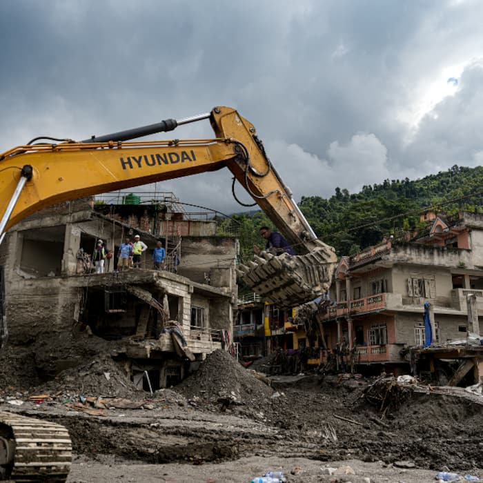 An excavator clears mud, sludge, and debris from damaged buildings along the Trishuli River, at Devighat, in Nuwakot district