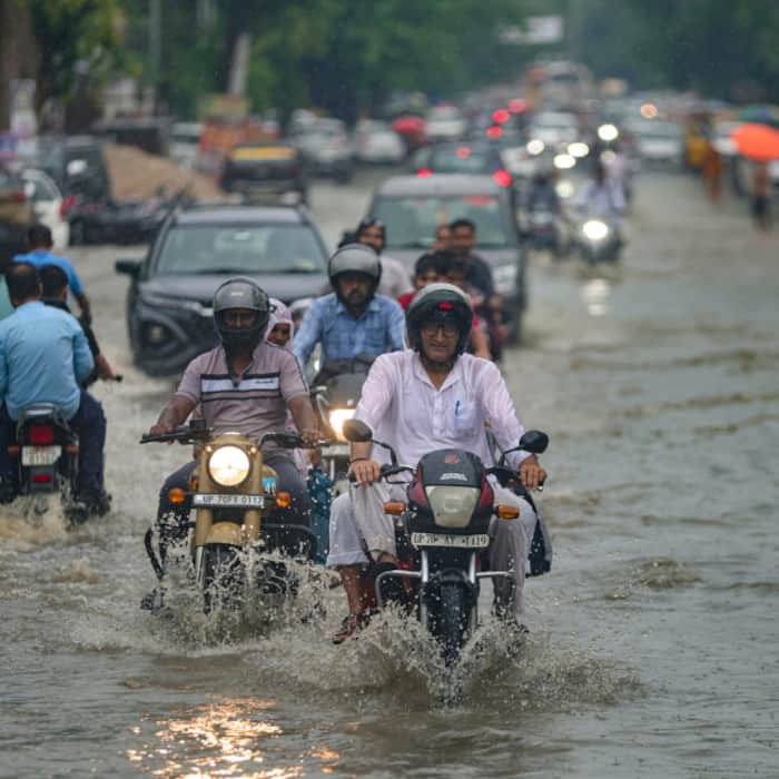 Commuters make their way through a waterlogged road following heavy rain, in Prayagraj, Uttar Pradesh
