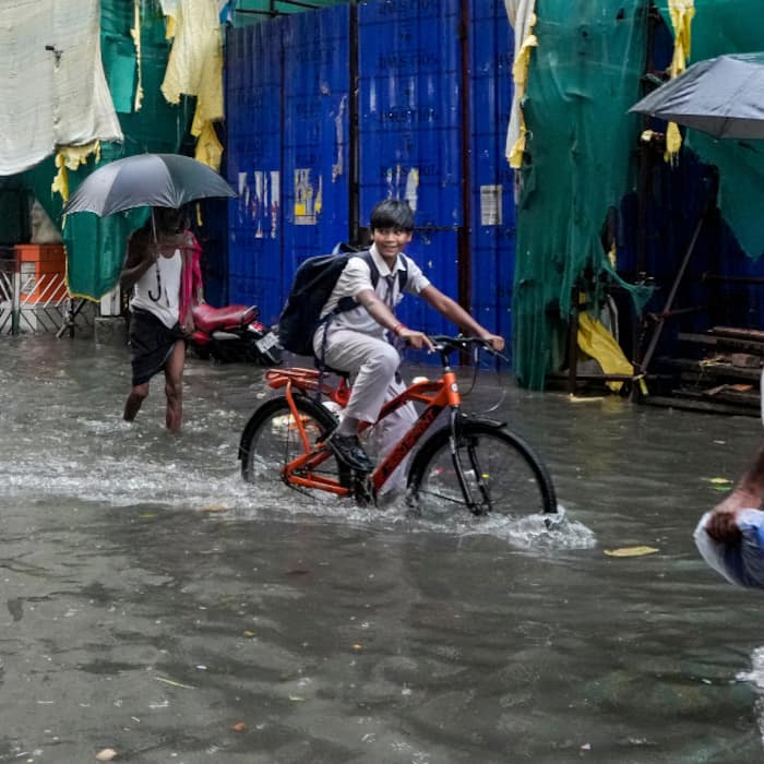 Commuters wade through a waterlogged road following heavy rain, in Kolkata
