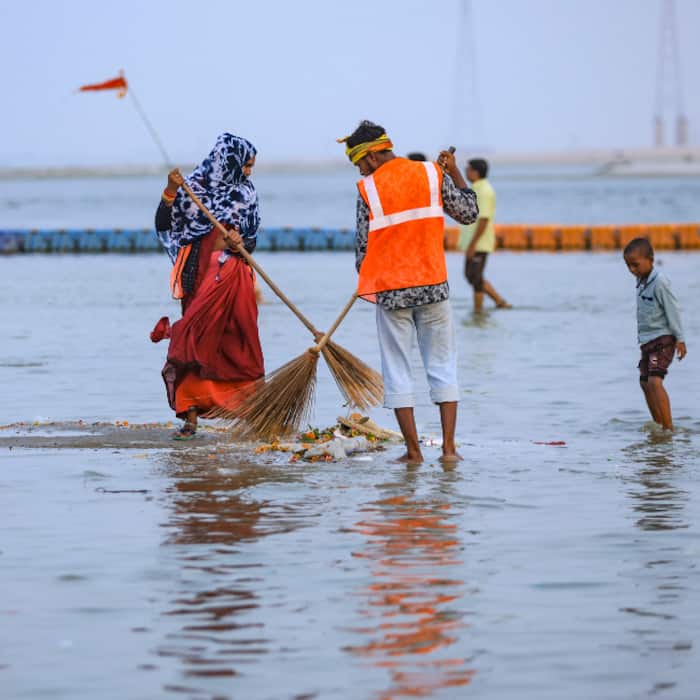Sanitation workers sweep the garbage from the submerged bank of the Sangam as the water level at the Sangam rises following monsoon rainfall, in Prayagraj
